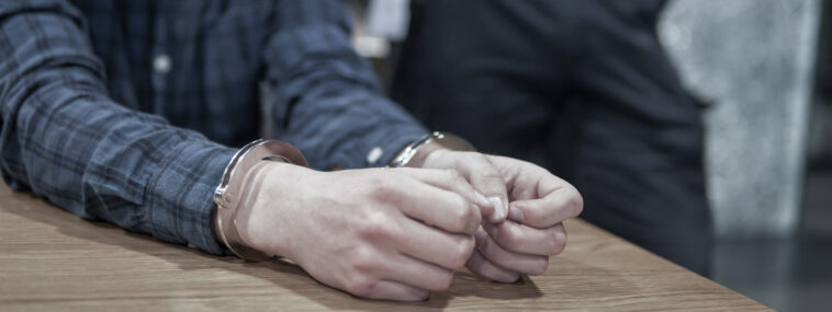 Criminal arrested and handcuffed while police grab shoulders.